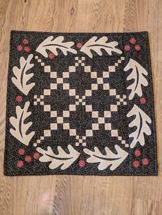 a black and white quilt with leaves on it sitting on top of a wooden floor