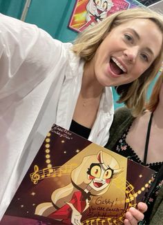 two women pose for the camera while holding up an animation book with cartoon characters on it