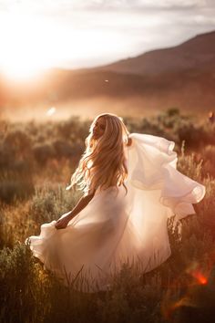 a woman in a white dress is walking through the grass with her hair blowing in the wind