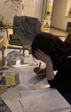 a woman sitting at a table with papers and pens in front of her, writing