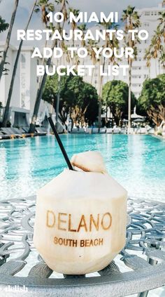 a drink sitting on top of a metal table next to a swimming pool with palm trees in the background