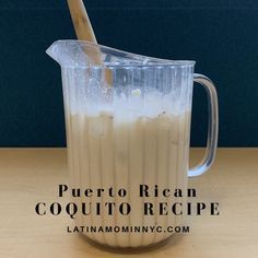 a pitcher filled with liquid sitting on top of a wooden table next to a spoon