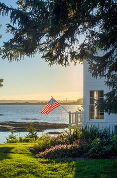 an american flag is flying in front of a house by the water at sunset or sunrise