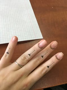 two fingers with small tattoos on them sitting next to a piece of paper and pen