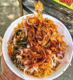 a person holding a white bowl filled with different types of food on top of it