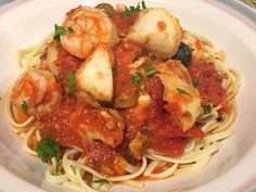 a white plate topped with pasta covered in sauce and shrimp on top of tomato sauce