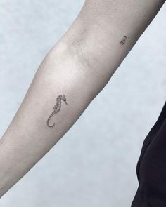 a woman's arm with a tiny seahorse tattoo on it