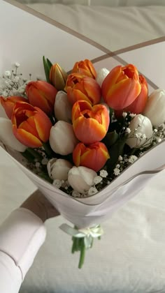 a bouquet of tulips and baby's breath in a white vase on a bed