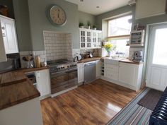 a kitchen with wood flooring and white cabinets is shown in this image, there is a large clock on the wall above the stove