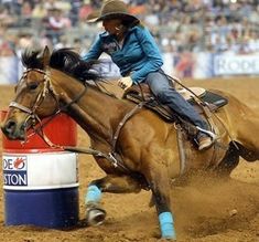 a woman riding on the back of a brown horse next to a red and white barrel