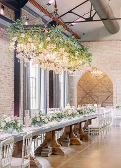 a long table with white flowers and greenery hanging from the ceiling