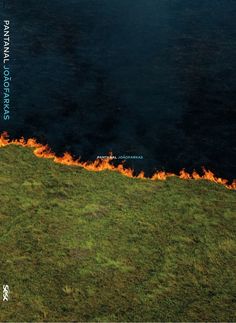 an aerial view of the fire burning on top of a grassy hill next to a body of water