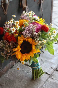 a bouquet of sunflowers and other flowers is sitting on the ground next to an open suitcase