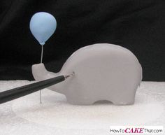 a small elephant with a balloon stuck to it's back in the snow by a pair of tongs