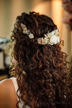 the back of a woman's head with curly hair and flowers in her hair