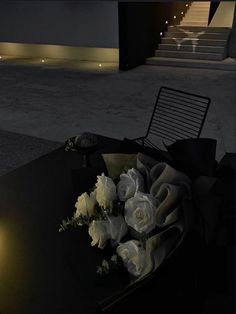 white roses are sitting on a black table in front of the stairs at night time