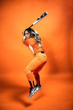 a woman in an orange outfit holding a baseball bat over her head while standing on one leg