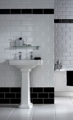 a white sink sitting next to a bath tub in a bathroom under a window with black and white tiles on the walls