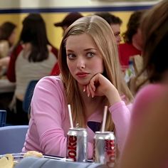 a woman sitting at a table with two sodas in front of her and another person behind her