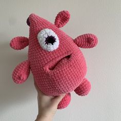 a hand holding a pink crocheted stuffed animal with large eyeballs on it's face