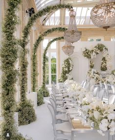 a long table is set with white flowers and greenery on the walls, along with hanging chandeliers