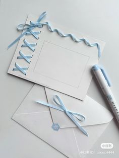 two pieces of paper with blue ribbon on them next to a pen and envelopes