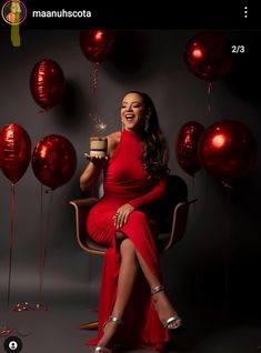 a woman in a red dress sitting on a chair holding a cupcake and balloons