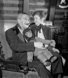 a man in a suit holding a monkey and smiling at the camera while sitting next to a young boy