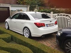 a white car parked in front of a house next to a driveway with hedges and bushes