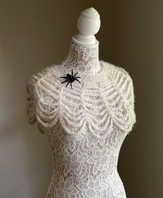 a white lace dress with a black spider on the front and bottom, sitting on a mannequin