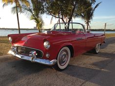 an old red car is parked on the side of the road near some palm trees