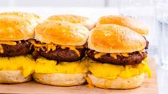 four hamburger sliders with cheese on them sitting on a cutting board next to a glass of water