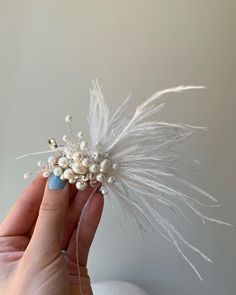 a hand holding a hair piece with white feathers and pearls