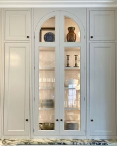 a white china cabinet with glass doors and plates