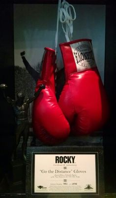 two red boxing gloves are on display in a glass case with a plaque underneath it