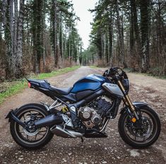 a blue motorcycle parked on the side of a dirt road in front of some trees