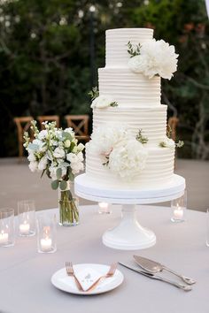 a wedding cake sitting on top of a table next to some flowers and silverware