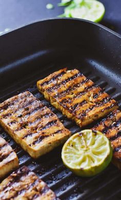 grilled food being cooked on a grill with lime slices and lemon wedges next to it