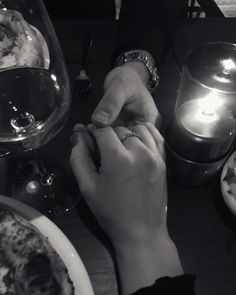 two people sitting at a table with food and candles in front of them, one holding the other's hand