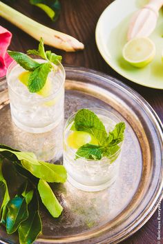 two glasses filled with ice and mint on top of a metal plate