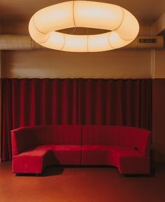 a red couch sitting in front of a window next to a curtained area with a round light above it