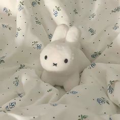 a white stuffed animal sitting on top of a bed covered in blankets and sheets with blue flowers