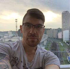 a man with glasses is taking a selfie in front of a cityscape