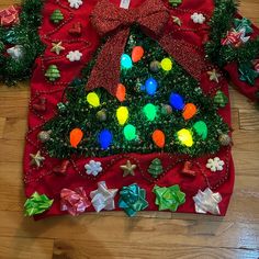 a red christmas sweater with lights and decorations on the front, sitting on a wooden floor