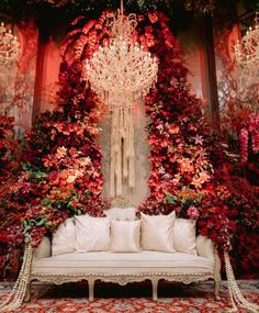 a white couch sitting under a chandelier surrounded by red flowers and greenery