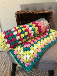 a crocheted blanket sitting on top of a gray chair next to a basket