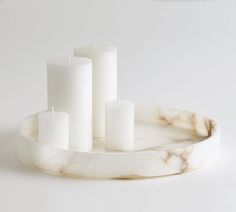 three white candles sitting on a marble tray