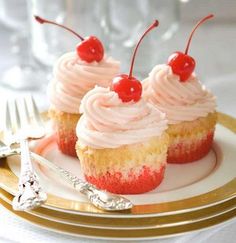 three cupcakes with pink frosting and cherries are on a white plate