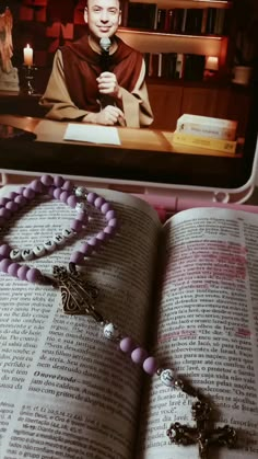 an open book with a rosary on top of it and a photo of a priest in the background