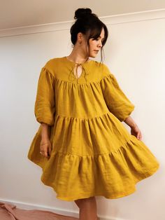 a woman in a yellow dress stands against a wall and looks off to the side